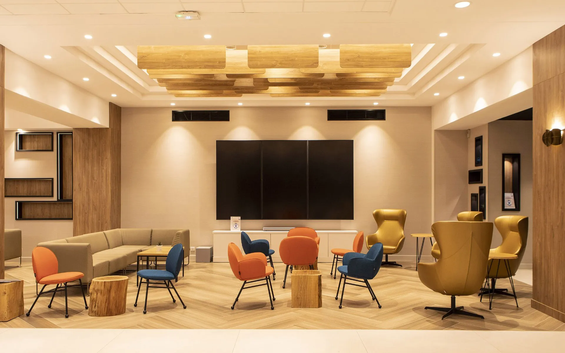 Salon aux fauteuils orange et bleu pétrole sous plafond en bois
